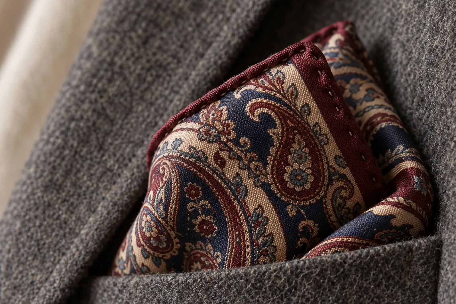 Close-up of a printed silk pocket square with a hand-rolled edge in a grey flannel breast pocket